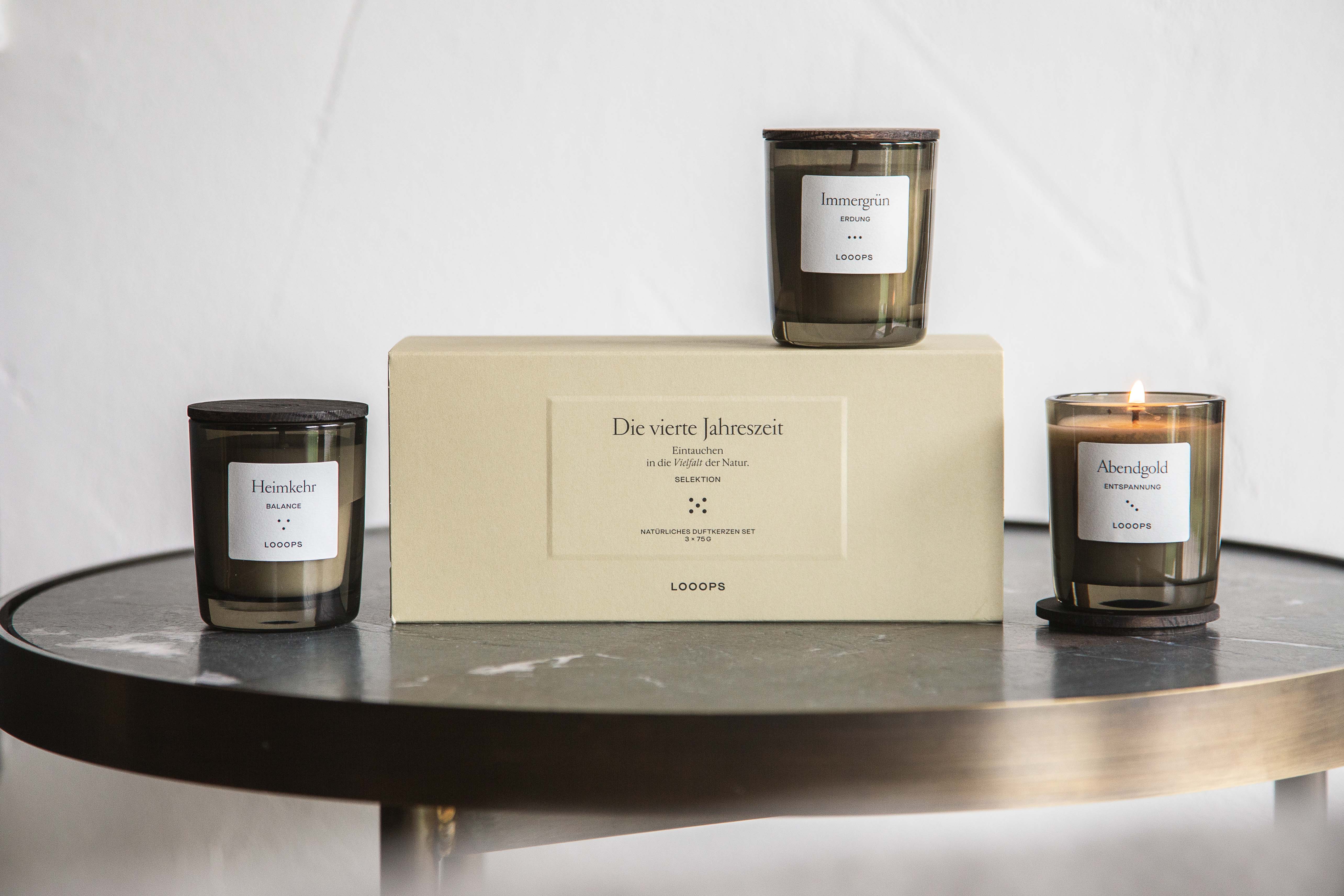 3 Loops Kerzen stehen neben bzw. auf der Looops Verpackung auf einem Beistelltisch.