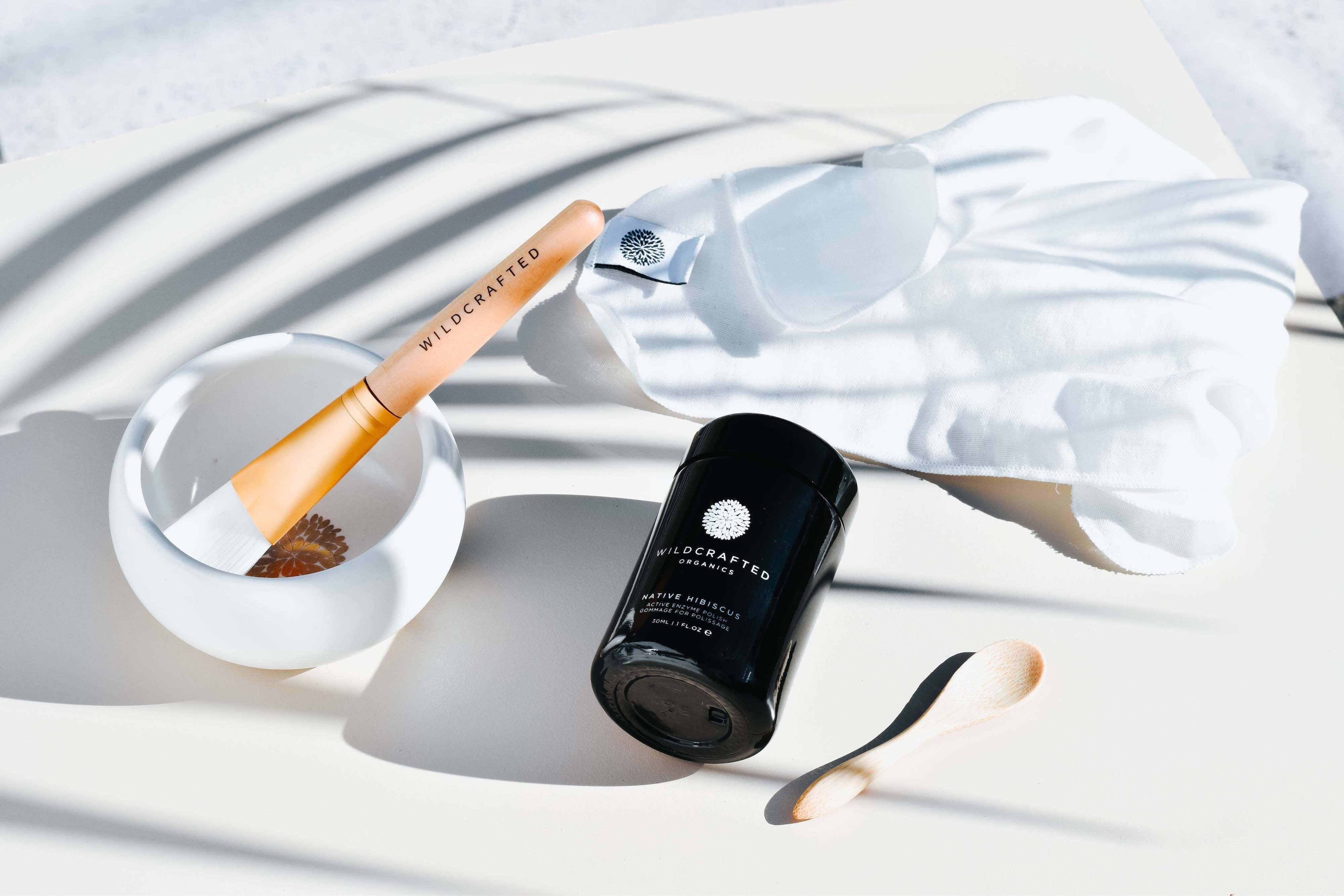 Wildcrafted Organics Native Hibiscus Tiegel liegt neben eine Schälchen mit Pinsel und Holzlöffelchen.