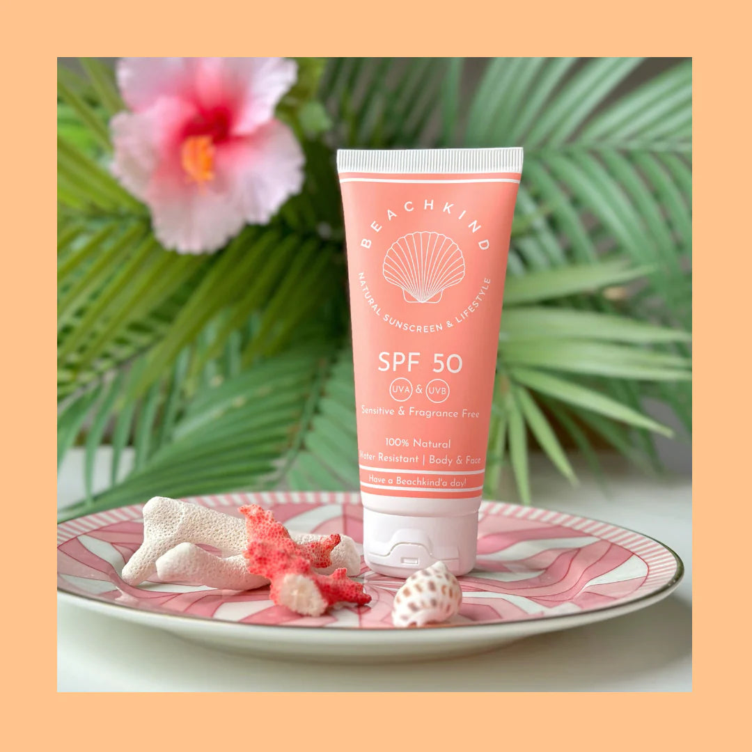 Beachkind Natzural Sunscreen SPF 50 stehend auf einem Teller mit rosanem Muster, dahinter verschwommen Farn und eine Blüte.