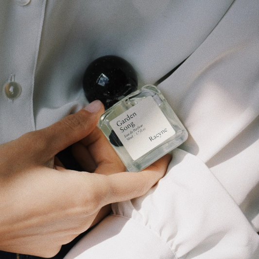 Garden Song Eau de Parfum von Racyne in einer Hand vor wei0er Bluse.