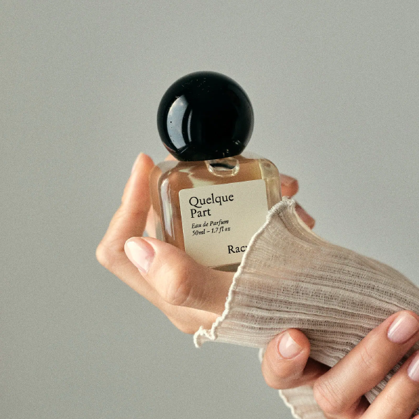 Quelque Part Eau de Parfum von Racyne - Glasflakon mit dunklem Verschluss in einer Hand mit Strickpullover.
