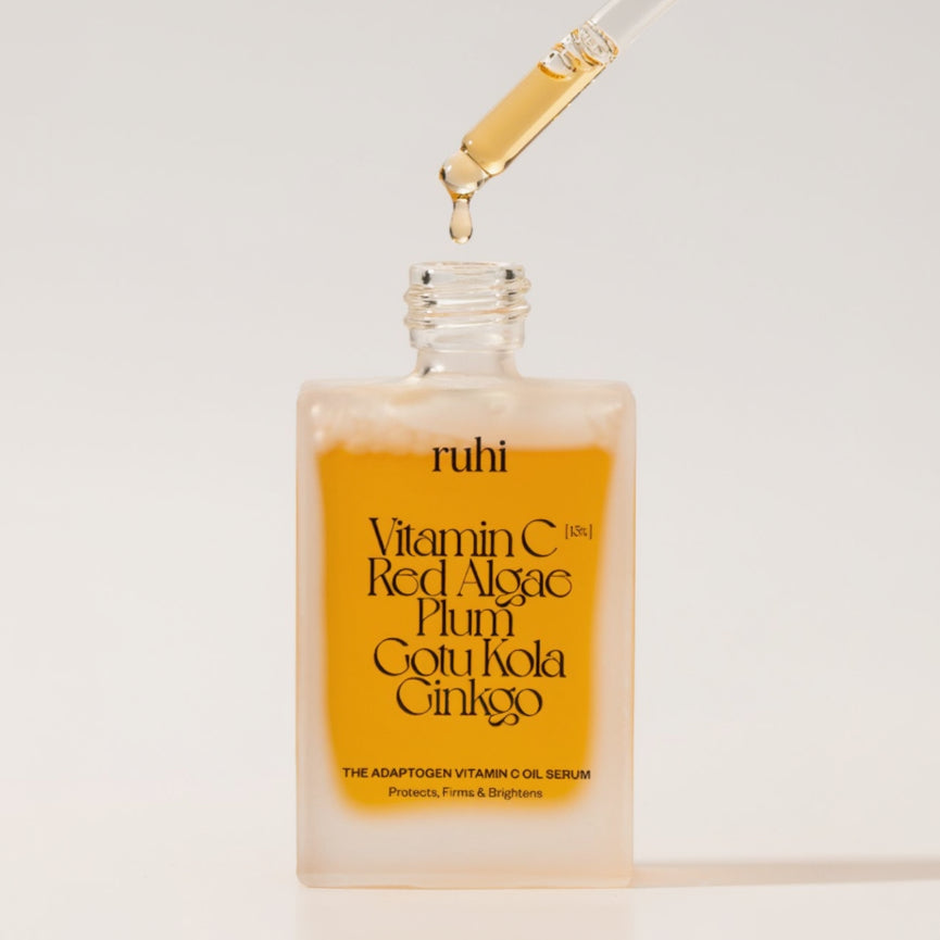 Eine gläserne Pipette tropft einen goldenen Tropfen des ruhi Vitamin C Öl-Serums zurück in die geöffnete, matte Glasflasche.