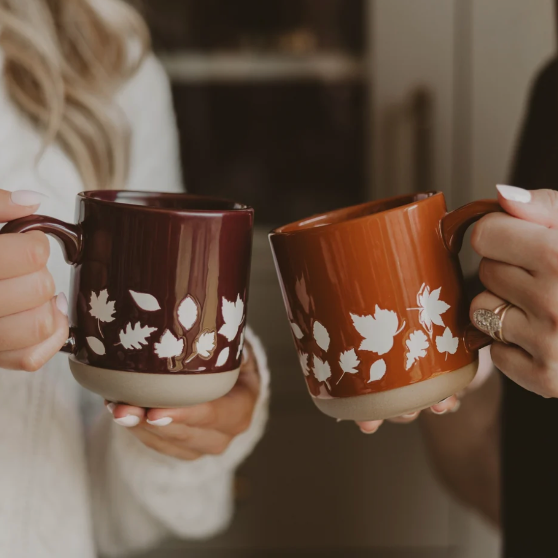 Sweet Water Decor Brown Fall Leaves Coffee Mug, gehalten neben Orange Leaves Coffee Mug.