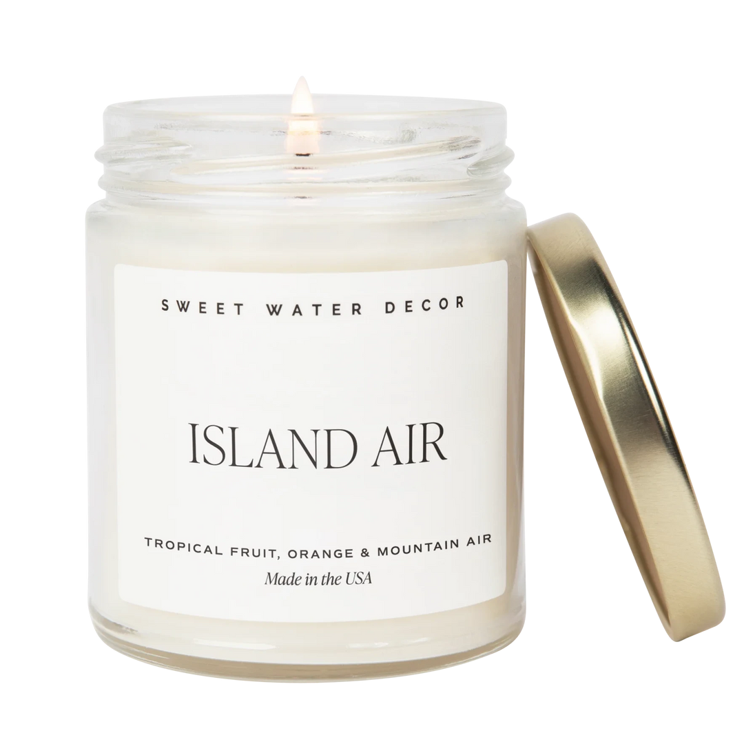 Kerzenglas "Island Air" von Sweet Water Decor, mit engelehntem goldenen Deckel, die Kerze ist entzündet, vor weißem Hintergrund. North Glow