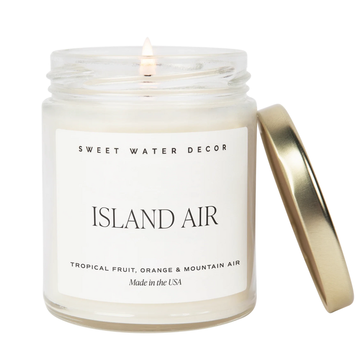 Kerzenglas "Island Air" von Sweet Water Decor, mit engelehntem goldenen Deckel, die Kerze ist entzündet, vor weißem Hintergrund.