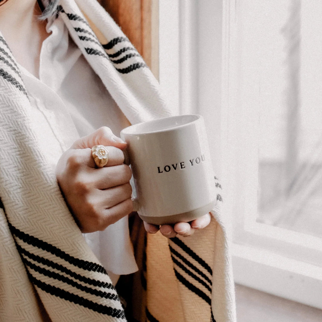 Kaffeetasse mit Aufschrift "Love you" wird von einer Frau mit Schal und Ring am Finger in den Händen gehlten