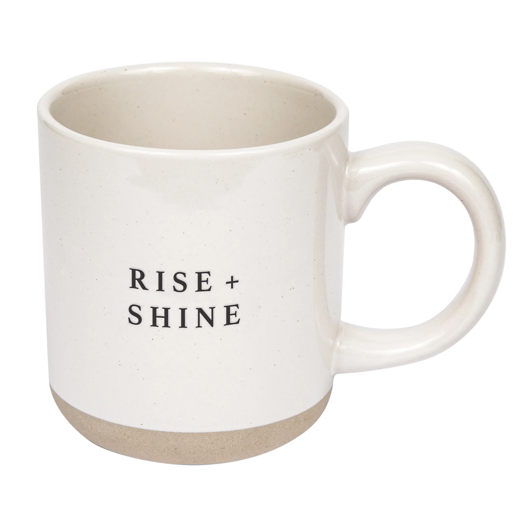 Cremefarbene Kaffee- oder Teetasse mit Aufschrift Rise and Shine von Sweet Water Decor vor weißem Hintergrund. North Glow