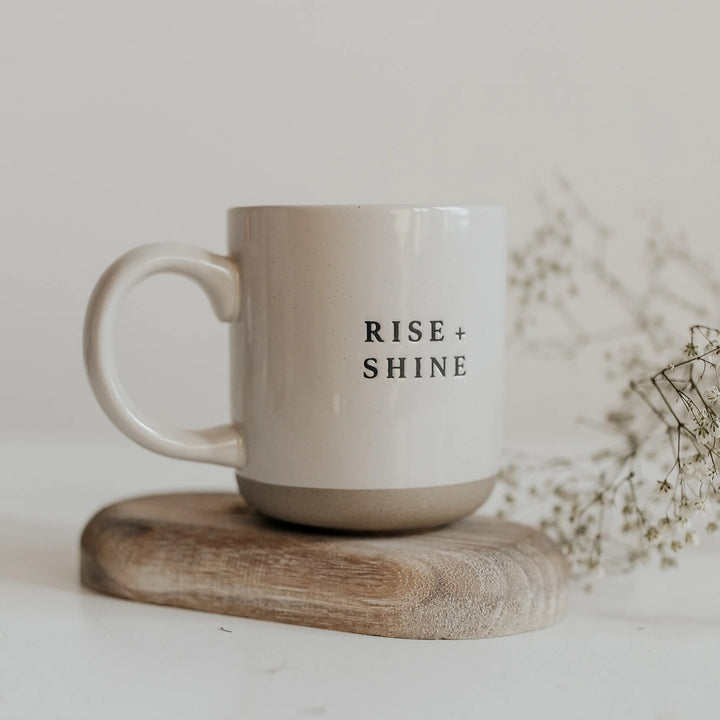 Cremefarbene Kaffee- oder Teetasse mit Aufschrift Rise and Shine von Sweet Water Decor auf einem Holzbrettchen
