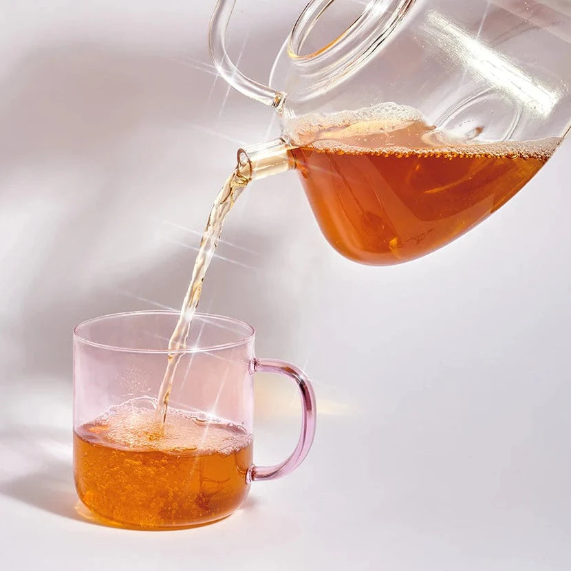 Glaskanne mit Tee von Cosmic Dealer gießt Tee in eine Glastasse. North Glow