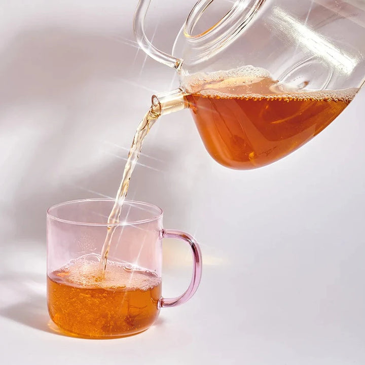 Glaskanne mit Tee von Cosmic Dealer gießt Tee in eine Glastasse.