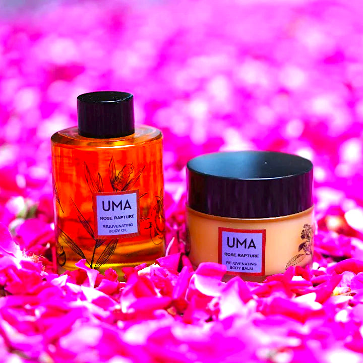 UMA Rose Rapture Body Balm Schraubglas und Öl Flasche stehen in einem Meer aus pinken Blütenblättern. North Glow