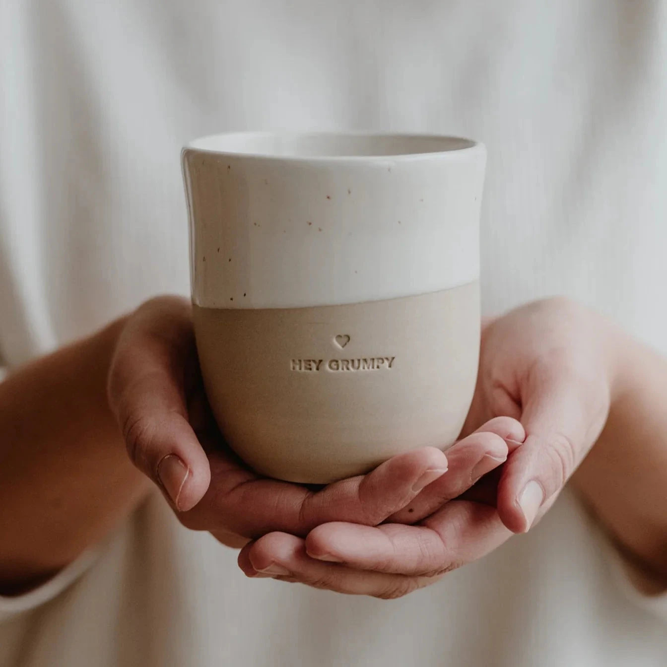 Becher "Hey Grumpy" von Eulenschnitt wird auf zwei Händen getragen.