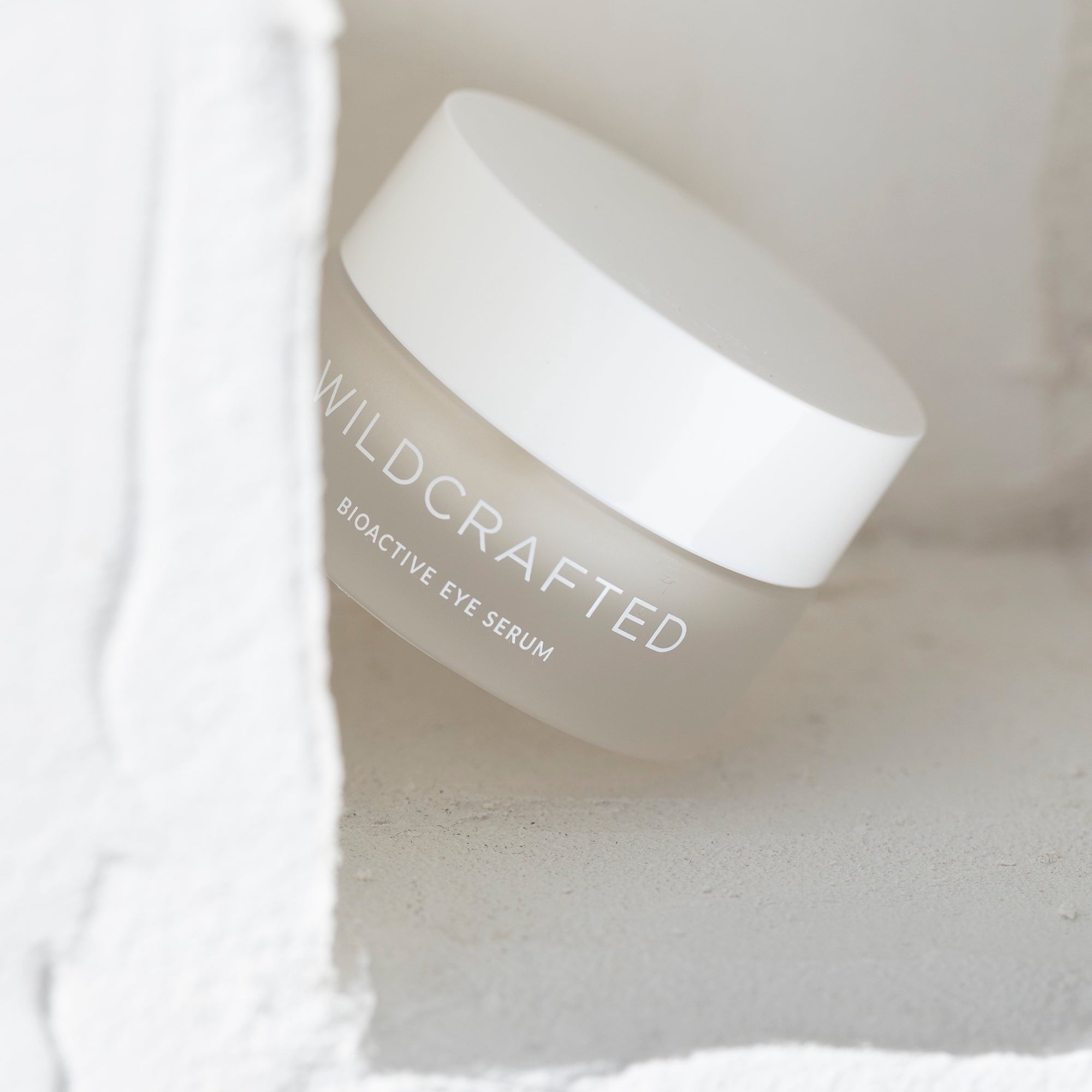 Milchglastiegel mit weißem Deckel Wildcrafted Bioactive Eye Serum vor hellem Hintergrund.