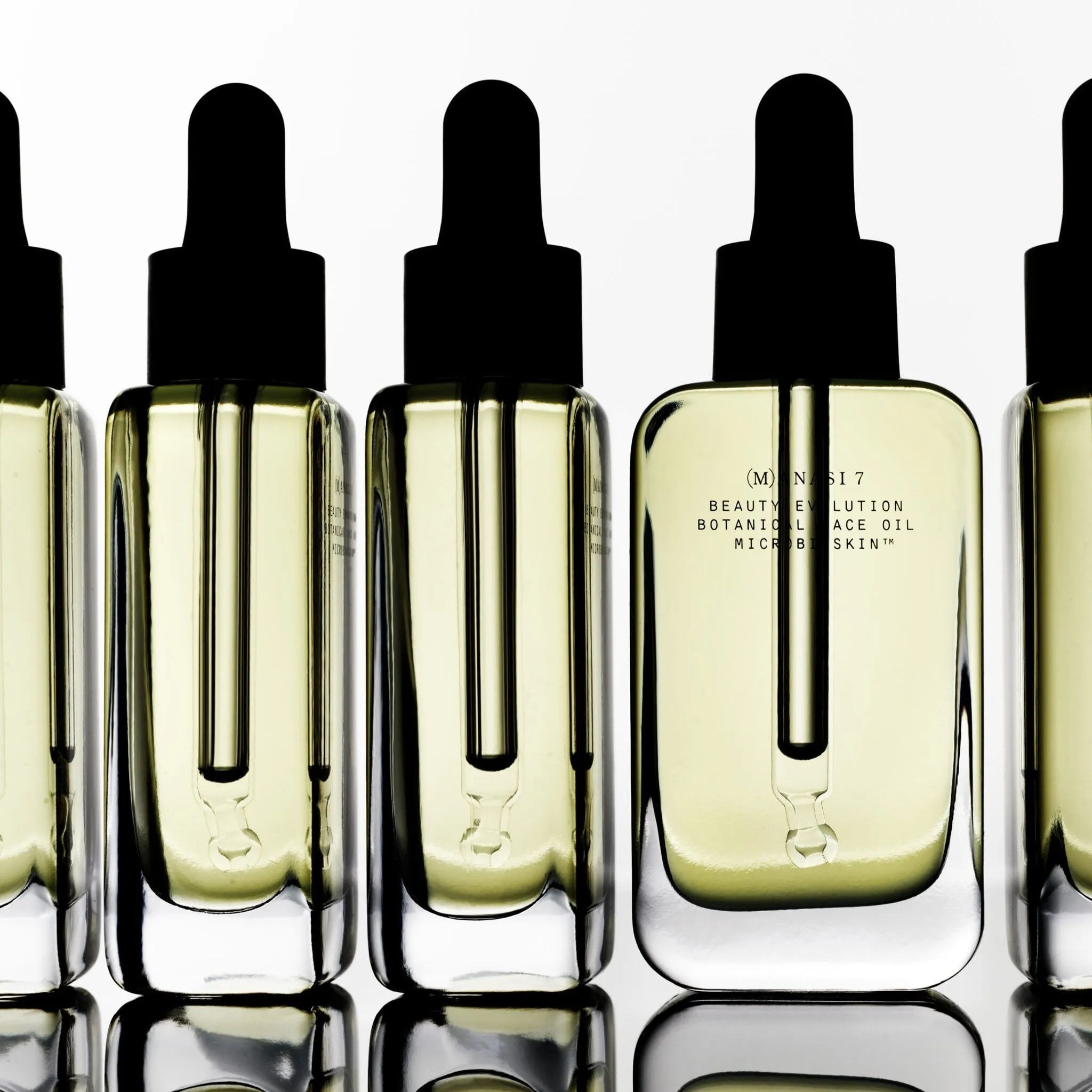 Manasi 7 Botanical Faceoil Armonia Flaschen aufgereiht stehen auf spiegelnden Untergrund.