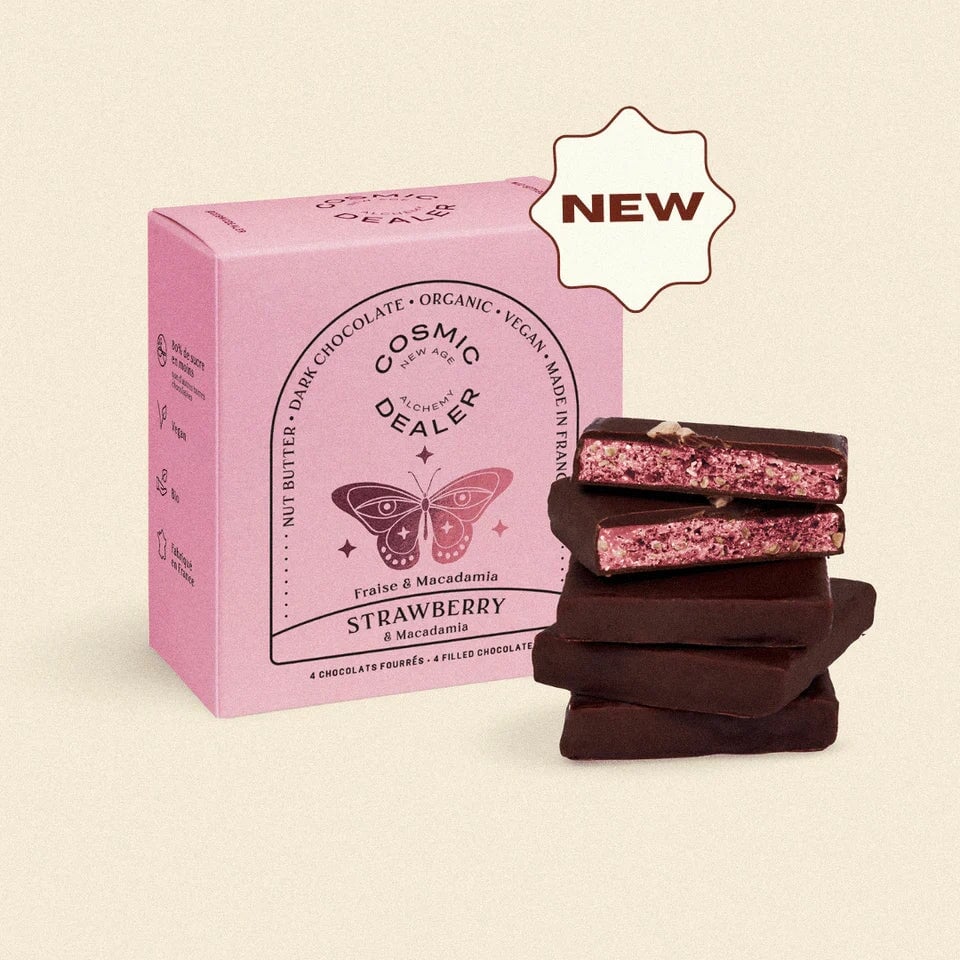 4er Box Cosmic Dealer Schokolade Strawberry & Macadamia mit gestapelten Schokoladentafeln davor.