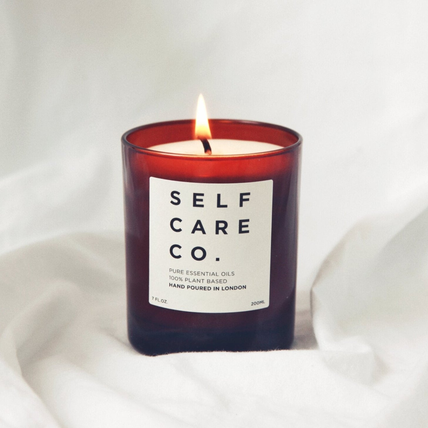 Braines Kerzenglas mit Aufschrift Self Care Co. steht auf weißem Tuch
