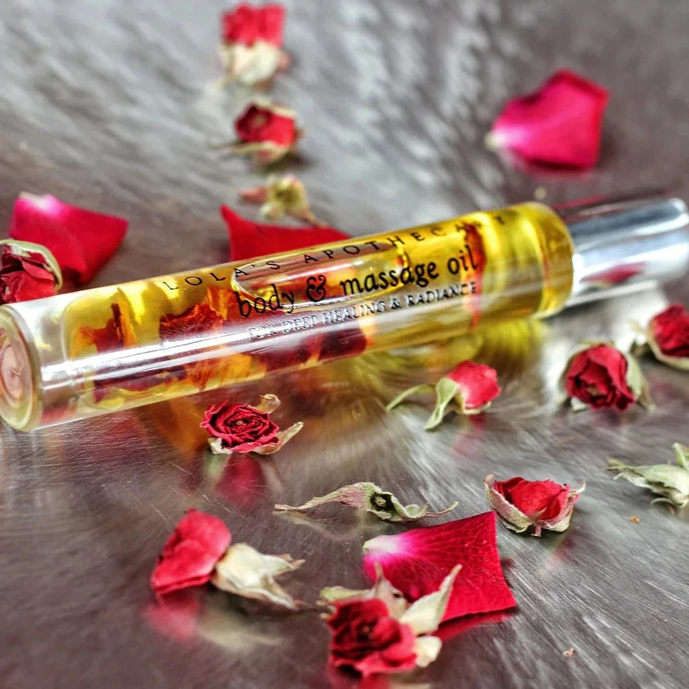 Lola's Apothecary Delicate Romance Deluxe Roll-On Glasflasche liegt auf Rosenblättern