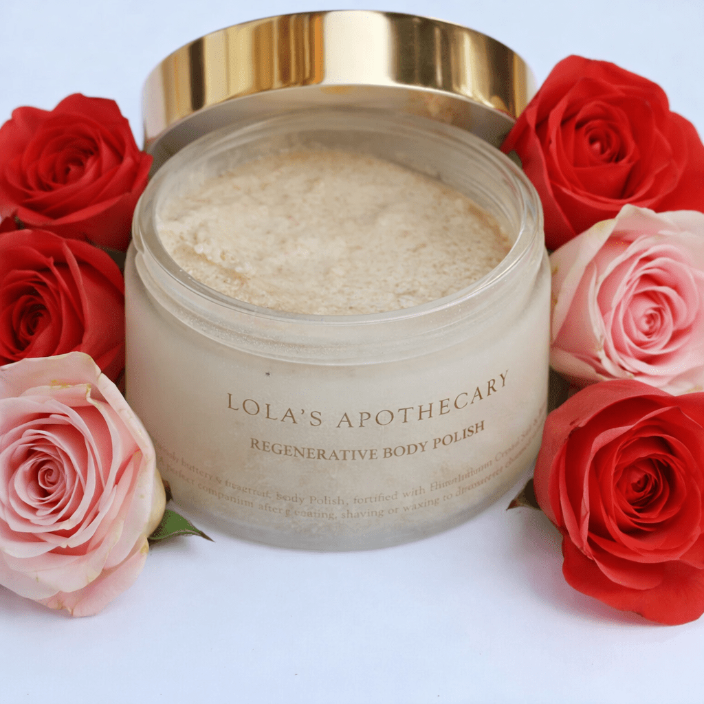 Geöffnetes Gefäß Lola's Apothecary Divine Grace Regenerative Body Polish, umgeben von Rosen.
