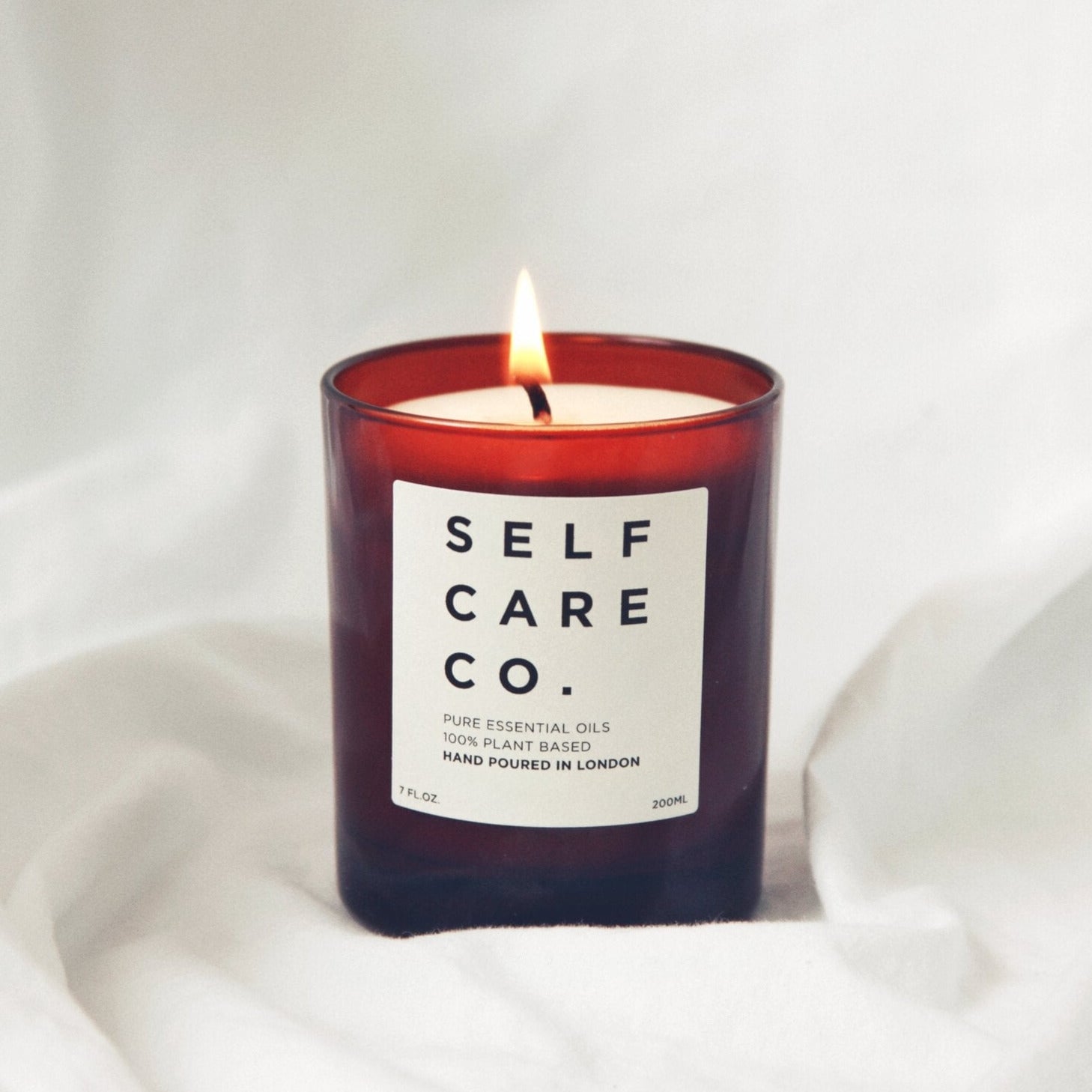 Braunes Kerzenglas mit Aufschrift Self Care Co. steht auf weißem Tuch