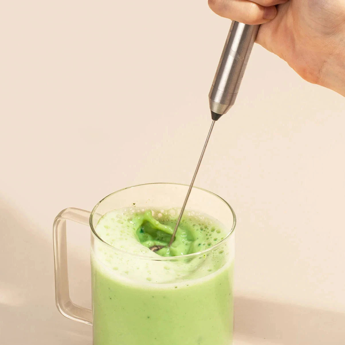 Hand hält den MATCHA & CO Electric Whisk beim Aufschäumen von grünem Matcha