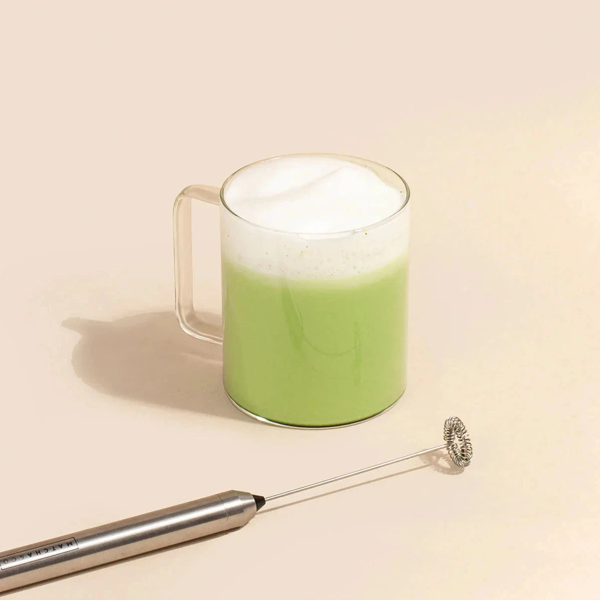 Elektrischer Matcha-Schäumer von MATCHA & CO liegt neben einer Tasse frisch zubereitetem Matcha-Tee