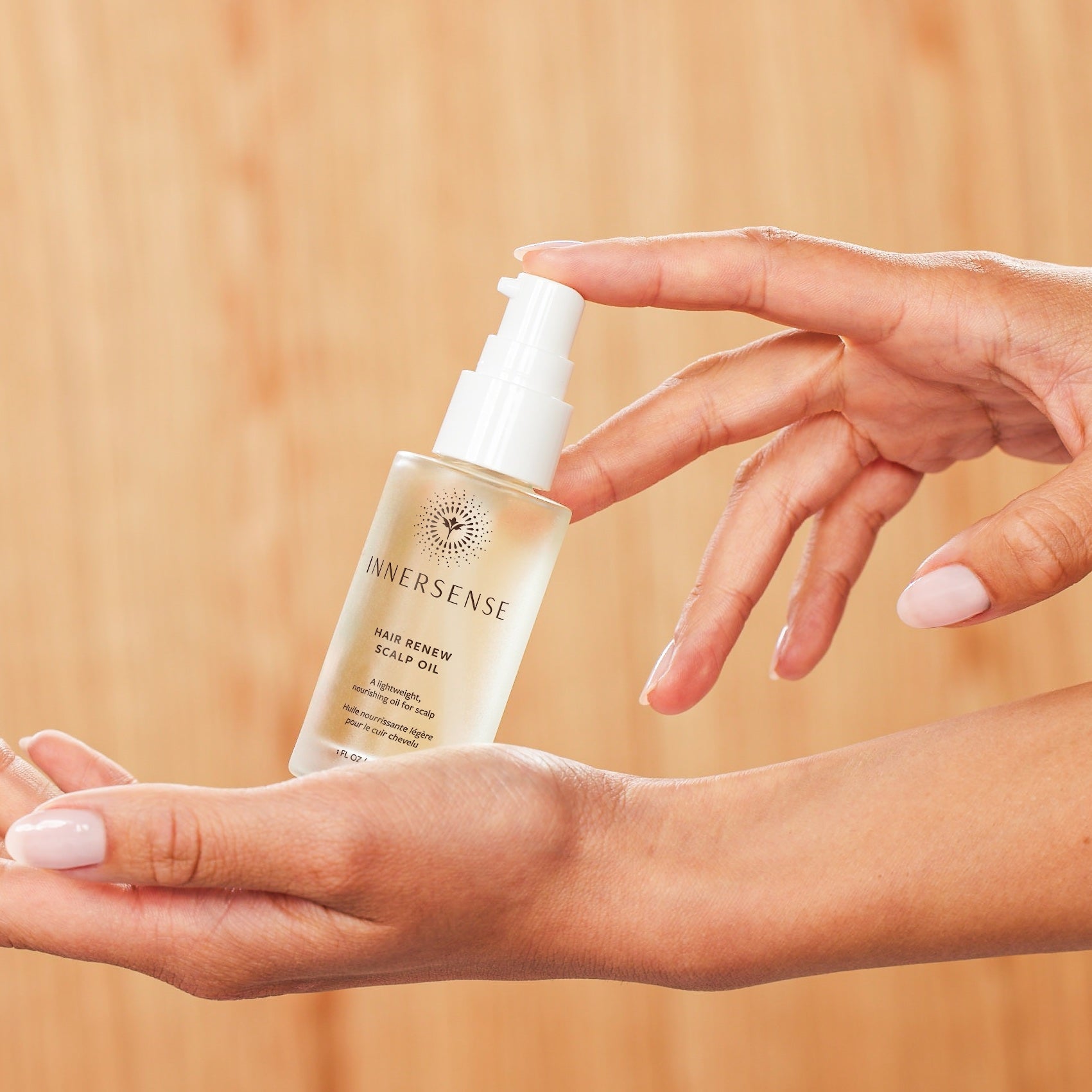 2 Hände halten Hair Renew Scalp Oil Flasche vor apricotfarbenem Hintergrund.