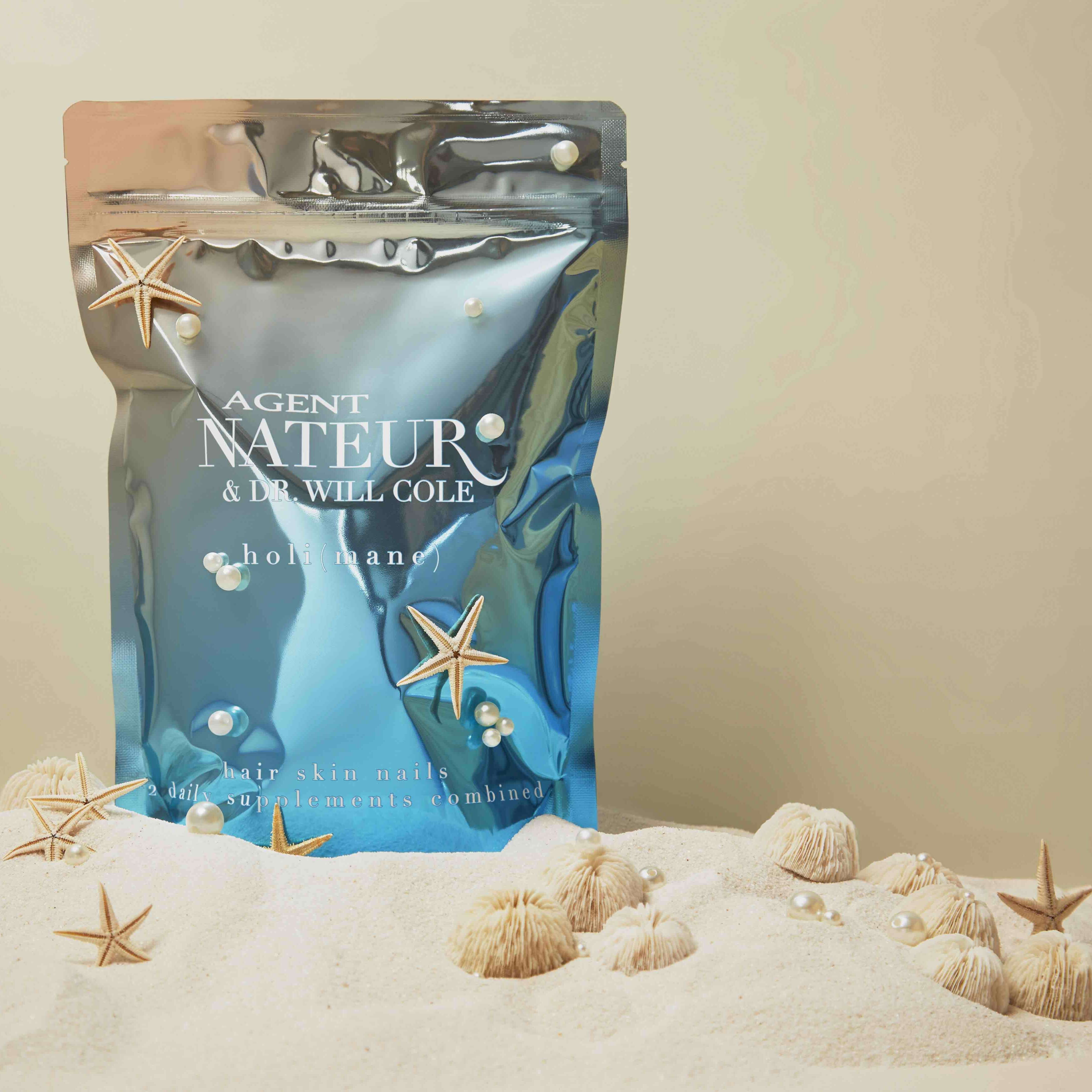 holi (mane) hair skin nails supplement Tüte vor beigem Hintergrund auf weißem Sand mit Seesternen und Perlen.