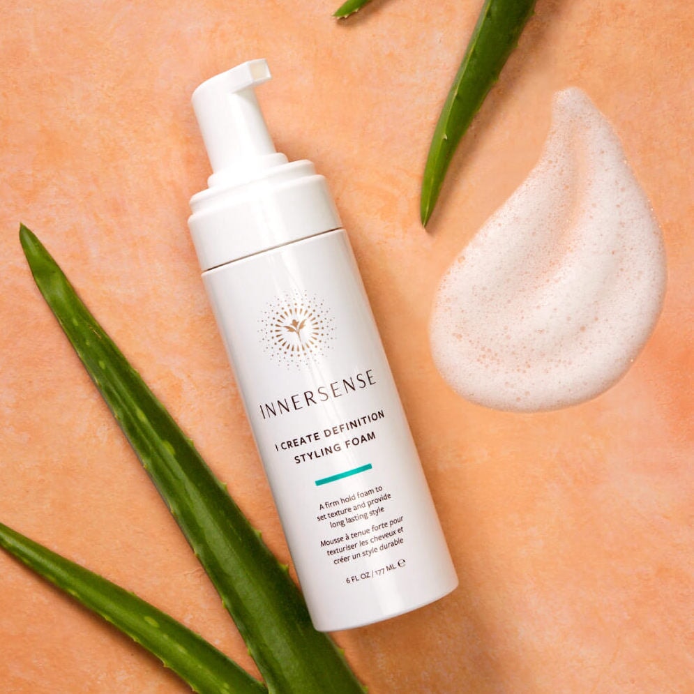 INNERSENSE I Create Definition Pumpflasche liegt auf apricotfarbenem Untergrund mit Texturbeispiel und Aloe Vera Blättern.