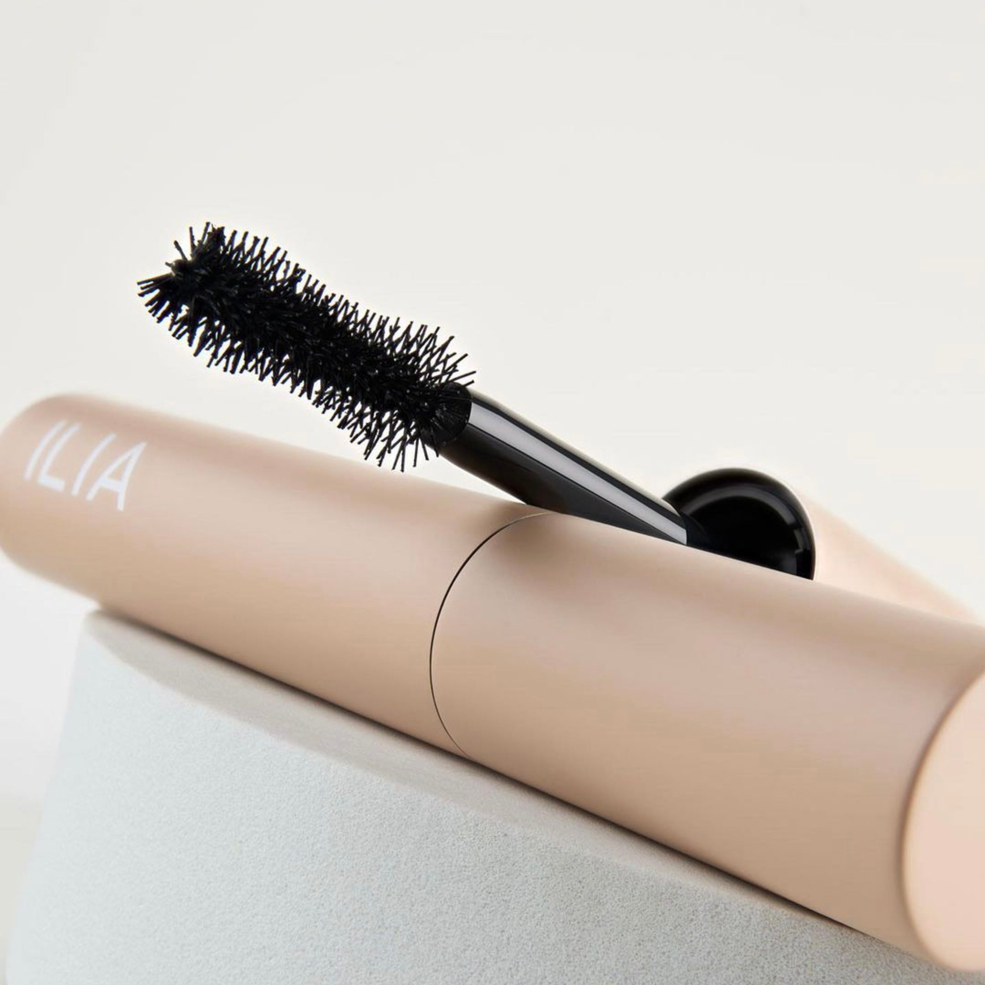 ILIA Fullest Voluminizing Mascarabürste lehnt an einer geschlossenen Mascara.