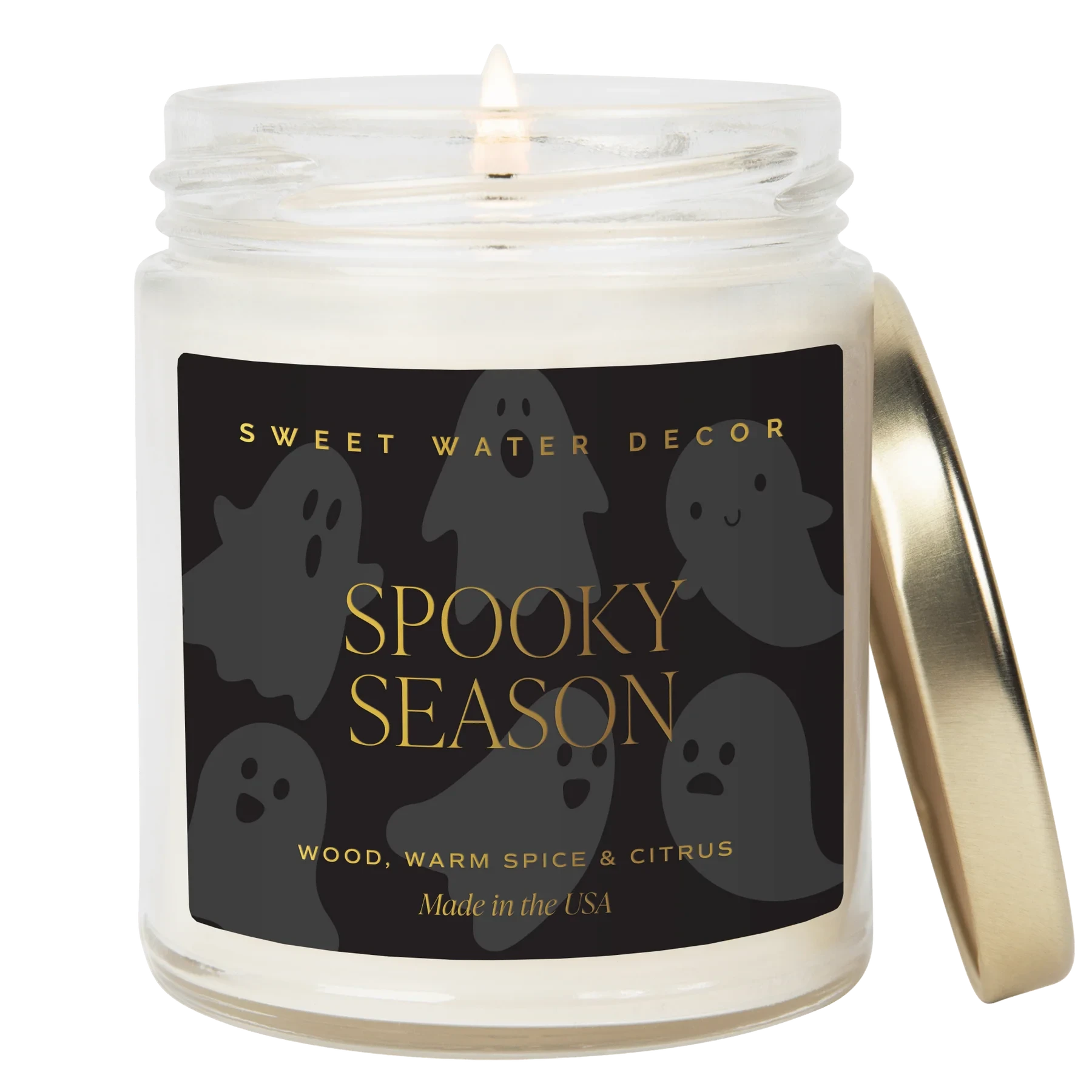 Brennende Kerze "Spooky Season" von Sweet Water Decor, daneben angelehnt ein goldener Deckel vor weißem Hintergrund.