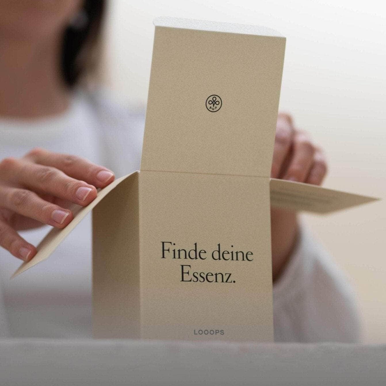 2 Hände öffnen die Verpackung einer Looops Duftkerze.