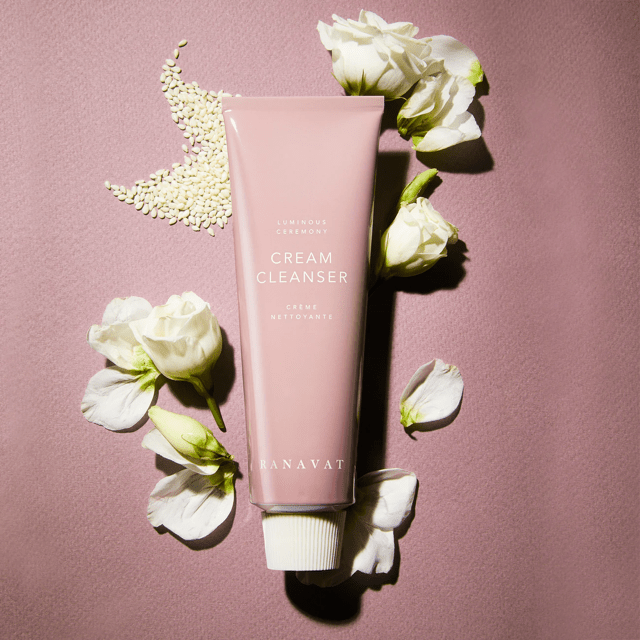 Ranavat Luminous Ceremony Cleanser auf rosa Hintergrund mit weißen Blüten und Sesam