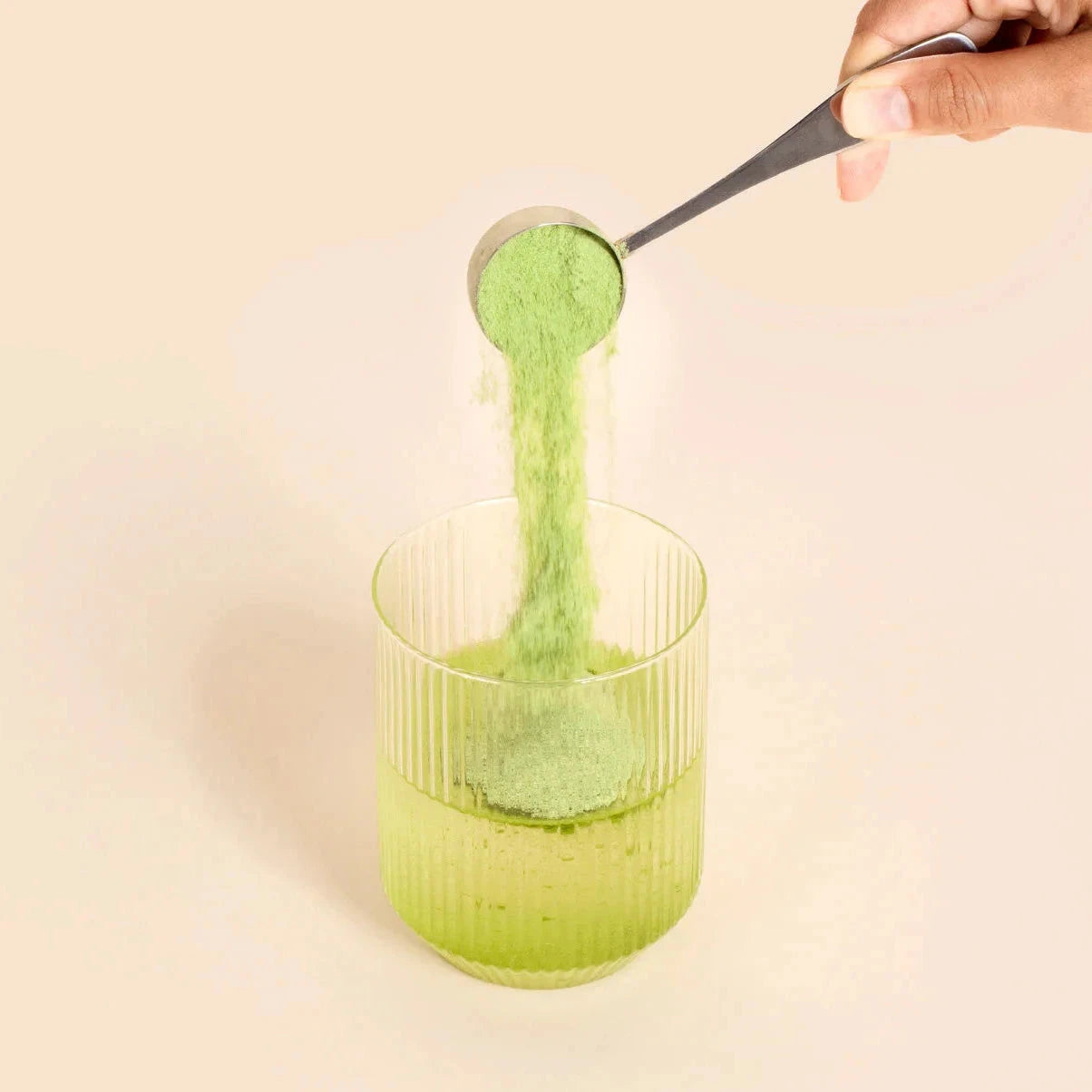 Dosierlöffel mit grünlichem Matcha-/Kollagenpulver von Matcha & CO über einem Trinkglas.