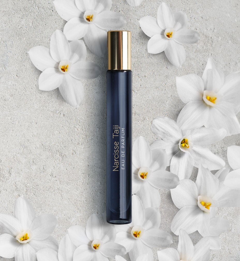 Dunkelblaues, schmales Glasgefäß mit goldenem Deckel "Narcisse Taiji" von Atelier Materi umgeben von Narzissen.