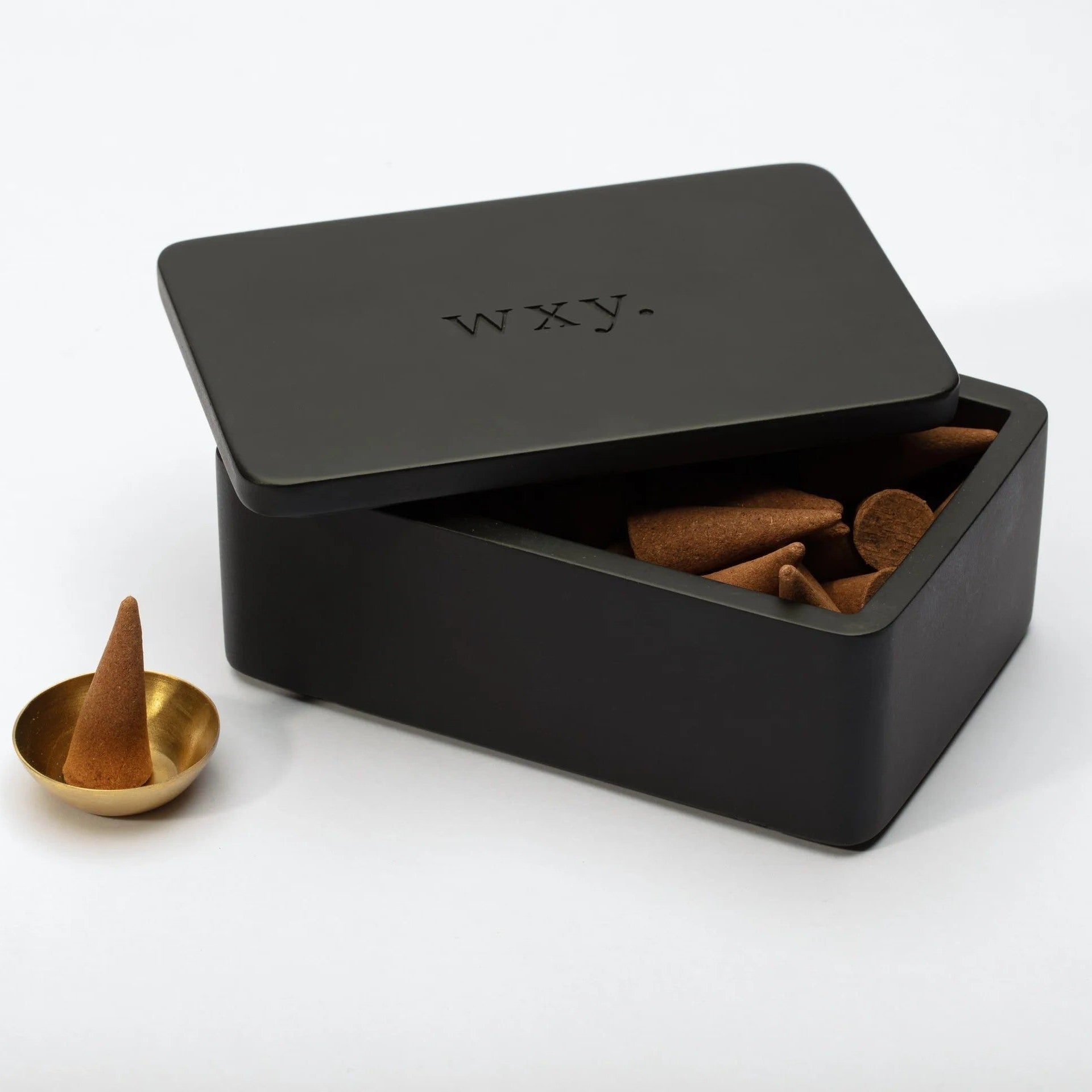 Halboffene owxy. Palo Santo Incense Cones Verpackung steht neben einem Messingschälchen mit einem Räucherkegel befüllt.