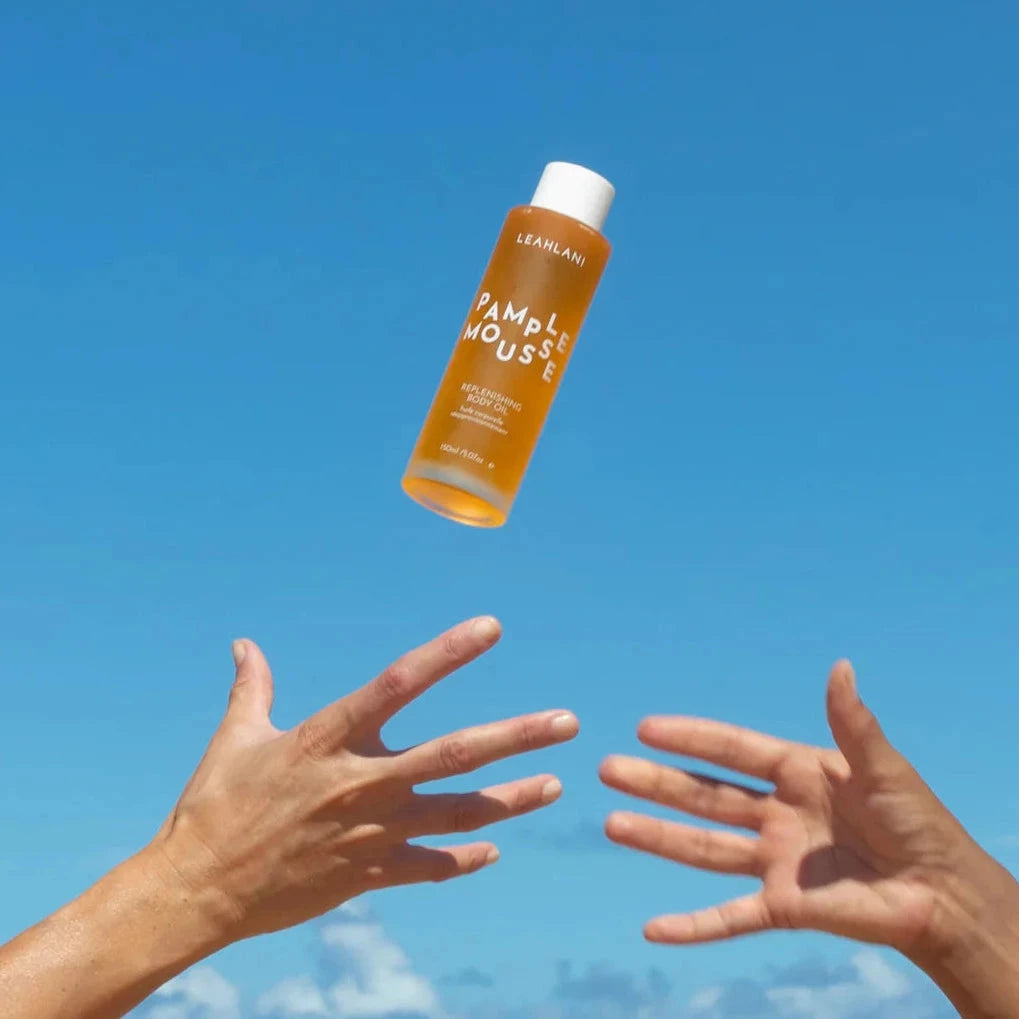 Leahlani Pamplemousse Body Oil wird durch die Luft geworfen und zwei Hände wollen es fangen.