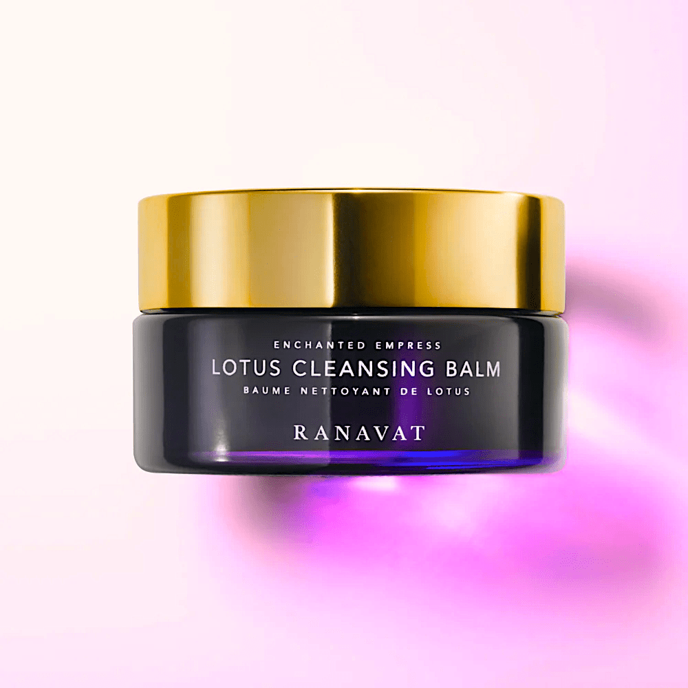 Dunkler Glastiegel Lotus Cleansing Balm mit goldenem Deckel von Ranavat steht vor hell pinkem, verschwommenem Hintergrund.
