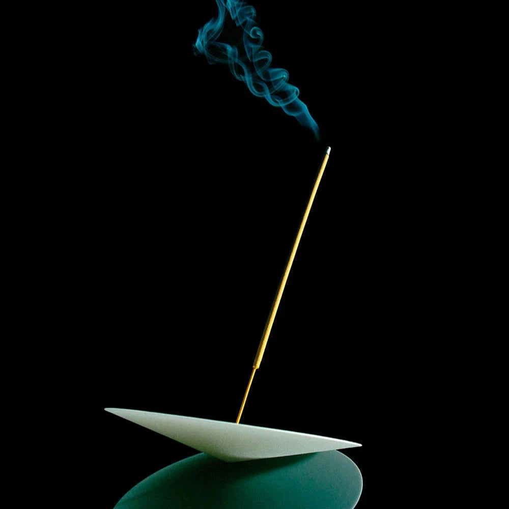 Qualmendes Räucherstäbchen in einer runden Halterung vor schwarzem Hintergrund.