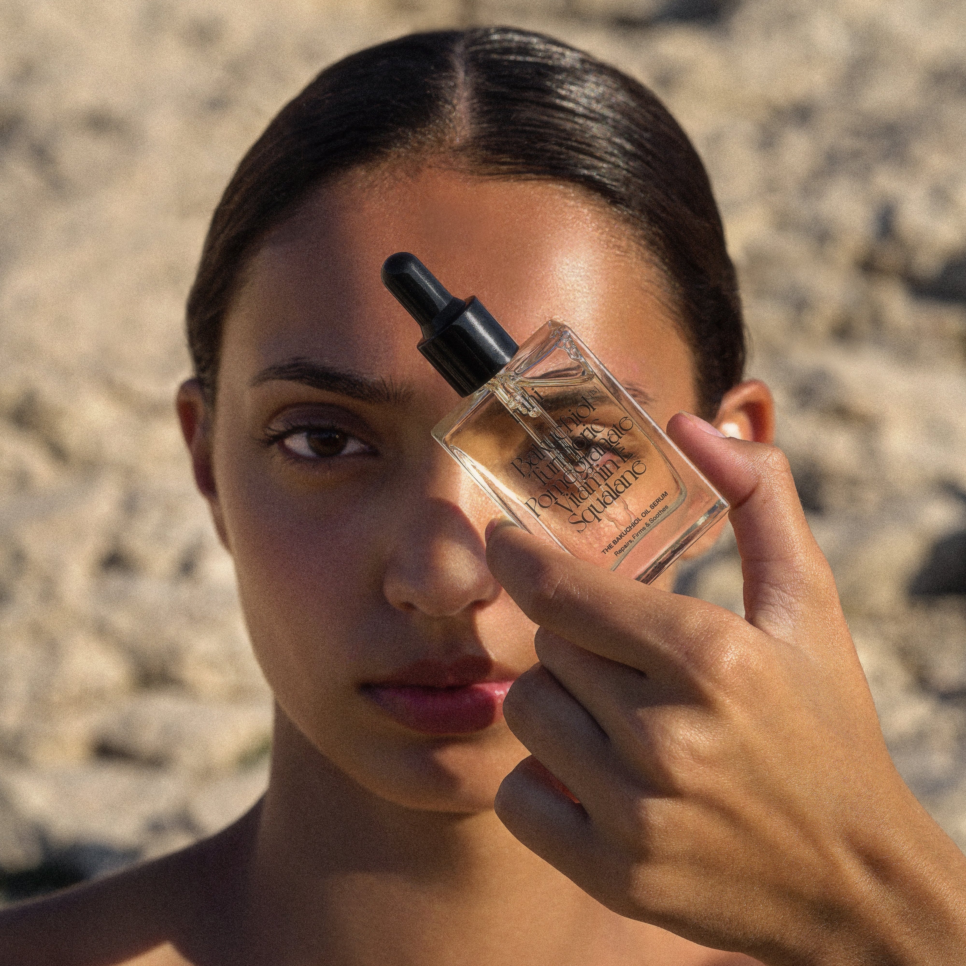 Eine Frau blickt in die Kamera und hält sich die Flasche des ruhi Bakuchiol Oil Serums vor das Gesicht.