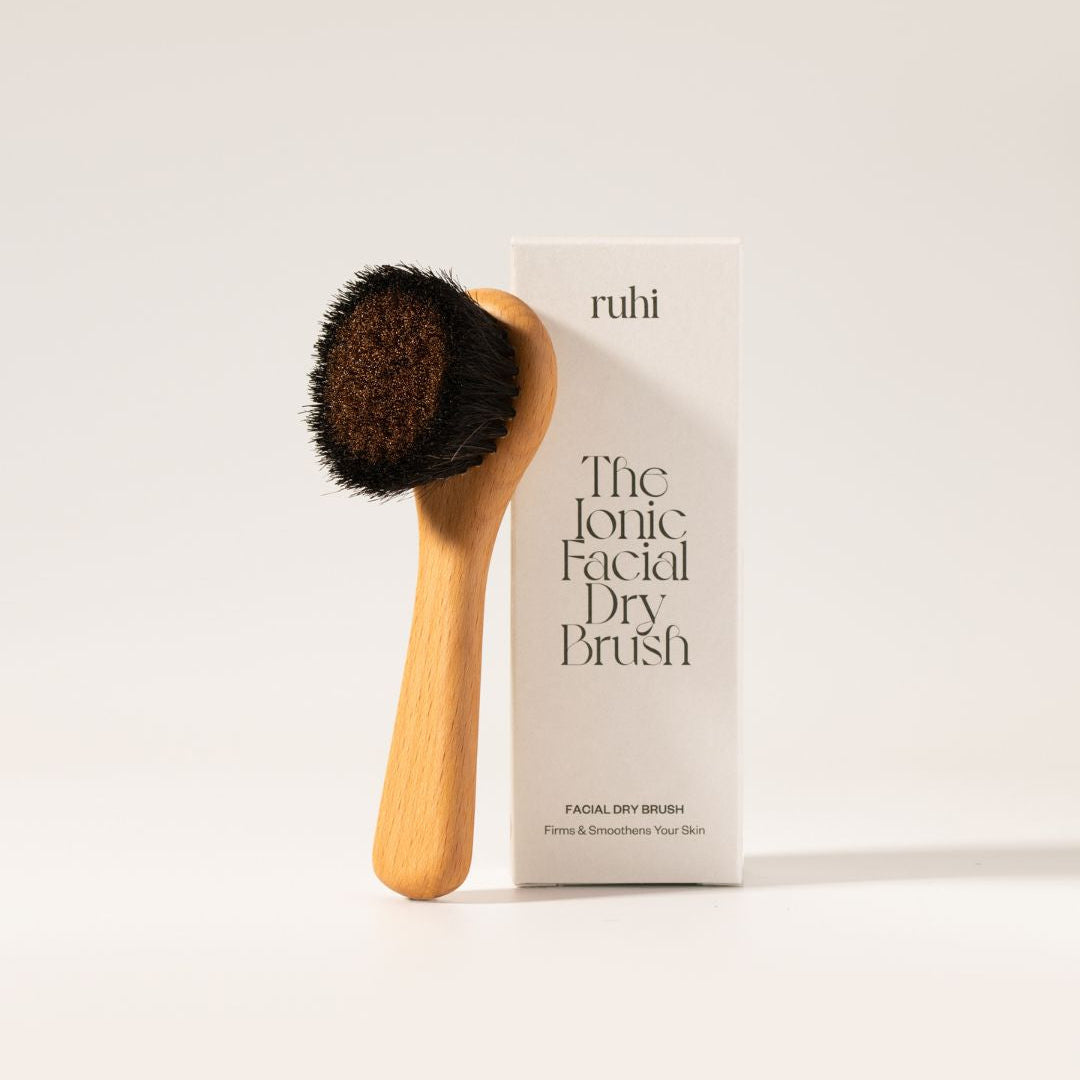 Die ruhi Ionic Facial Dry Brush aus Holz mit dunklen Borsten stehend neben ihrer weißen Produktverpackung.