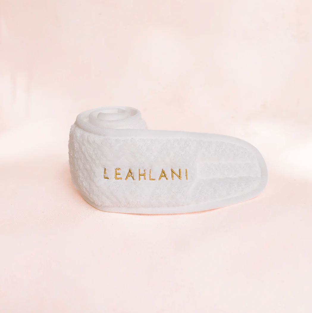 Weißes Stirnband eingerollt mit Aufschrift LEAHLANI vor zartrosa Hintergrund.