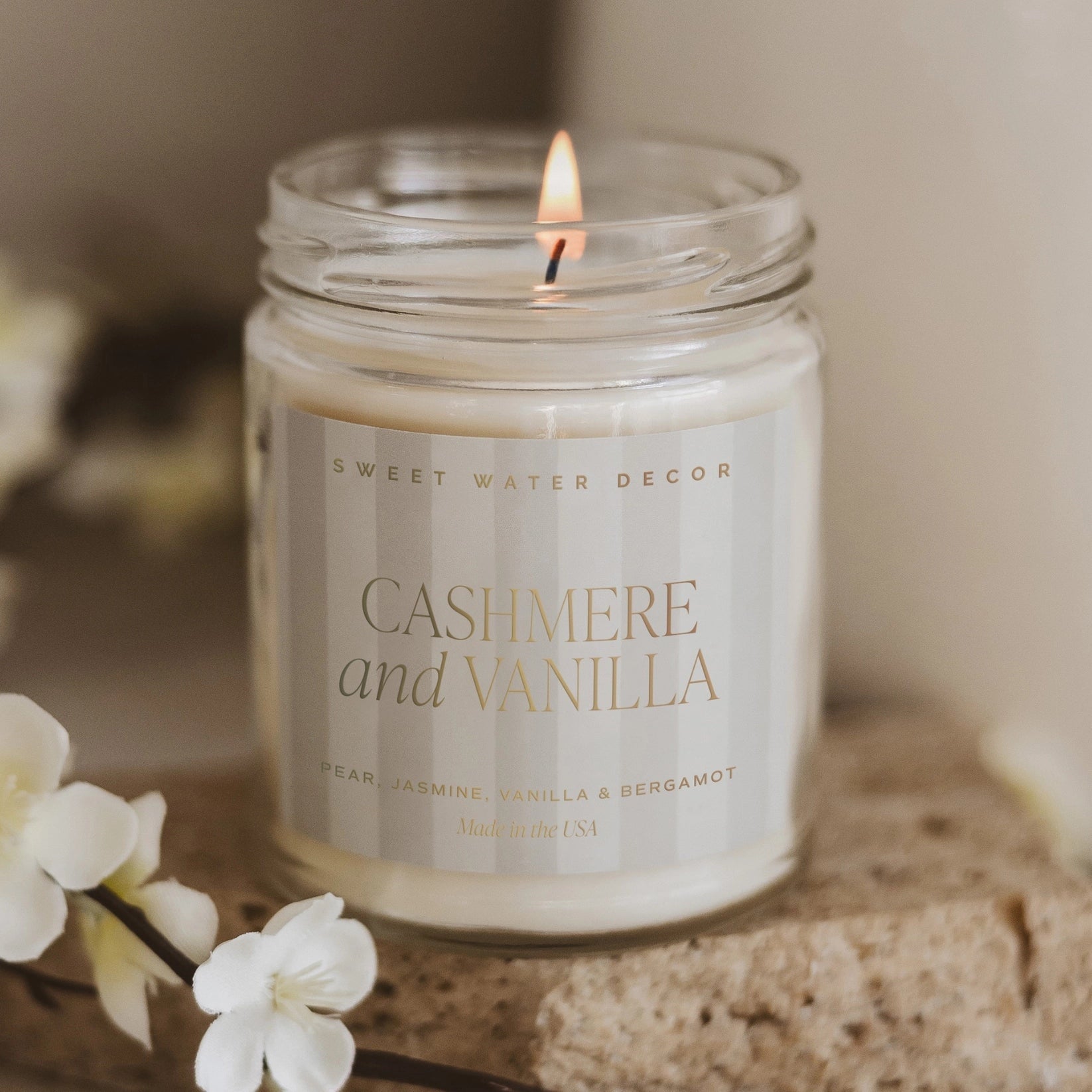 Brennende Sojawachskerze Cashmere and Vanilla steht nebnen einer blühenden Vanilleschote.