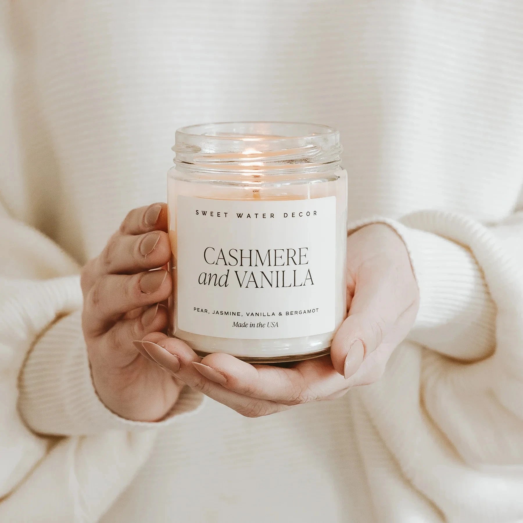 Zwei Hände halten eine brennende Sojawachskerze Cashmere and Vanilla.