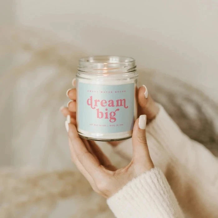 2 Hände halten eine brennende Sojawachskerze Dream Big von Swee Water Decor im Schraubglas fest.