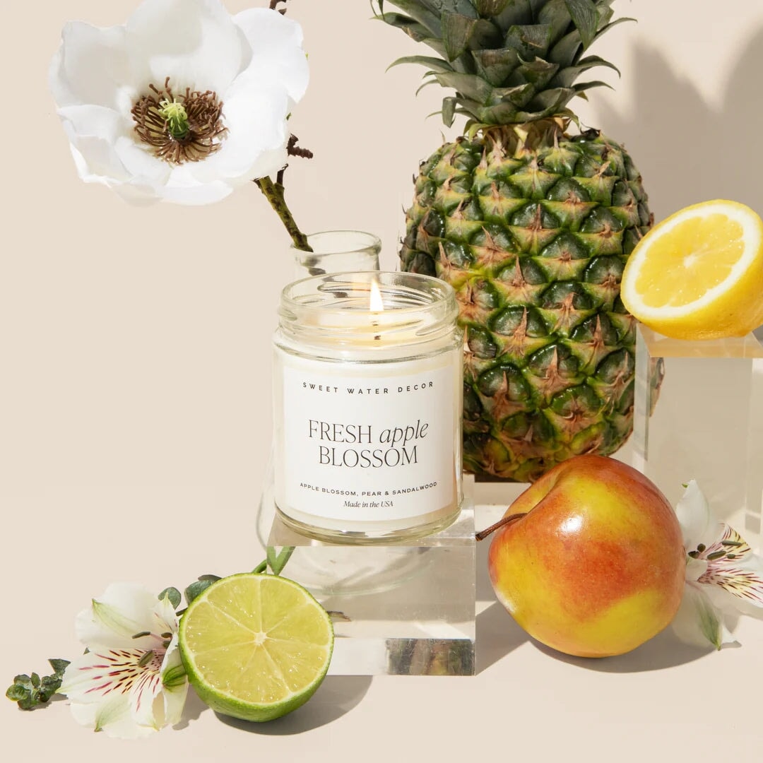 Offenes Duftkerzenglas Fresh Apple Blossom steht zwiwchen Früchten und Blüten.