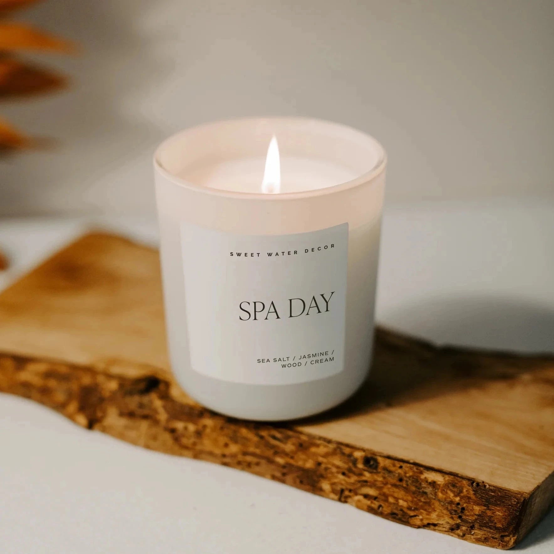 Cremefarbenes Kerzenglas mit Aufschrift "Spa Day" steht auf einem Holzbrett