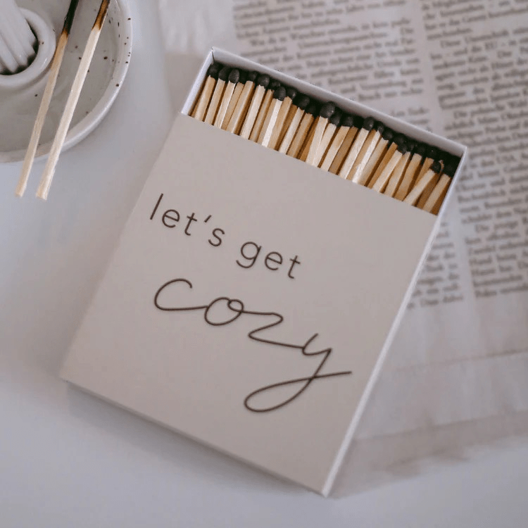 Leicht geöffnete Strichholzschachtel let's get cozy von Eulenschnitt liegt auf einer Zeitung, aus der Vogelperspektive.