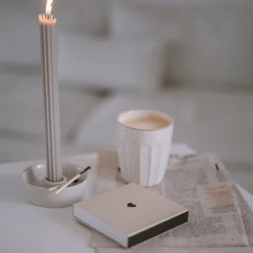 Strichholzschachtel let's get cozy von Eulenschnitt liegt auf einem Tischchen neben einem Becher Kaffee und einer brennenden Kerze.