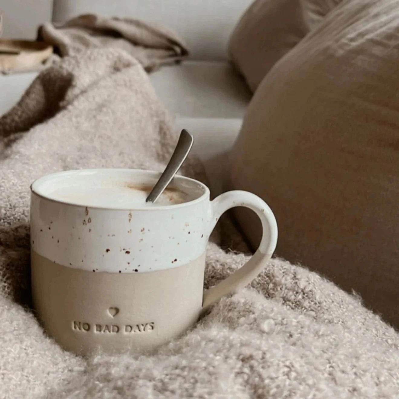 Tasse mit Prägung "no bad days" von Eulenschnitt steht auf cremefarbener Wolldecke.