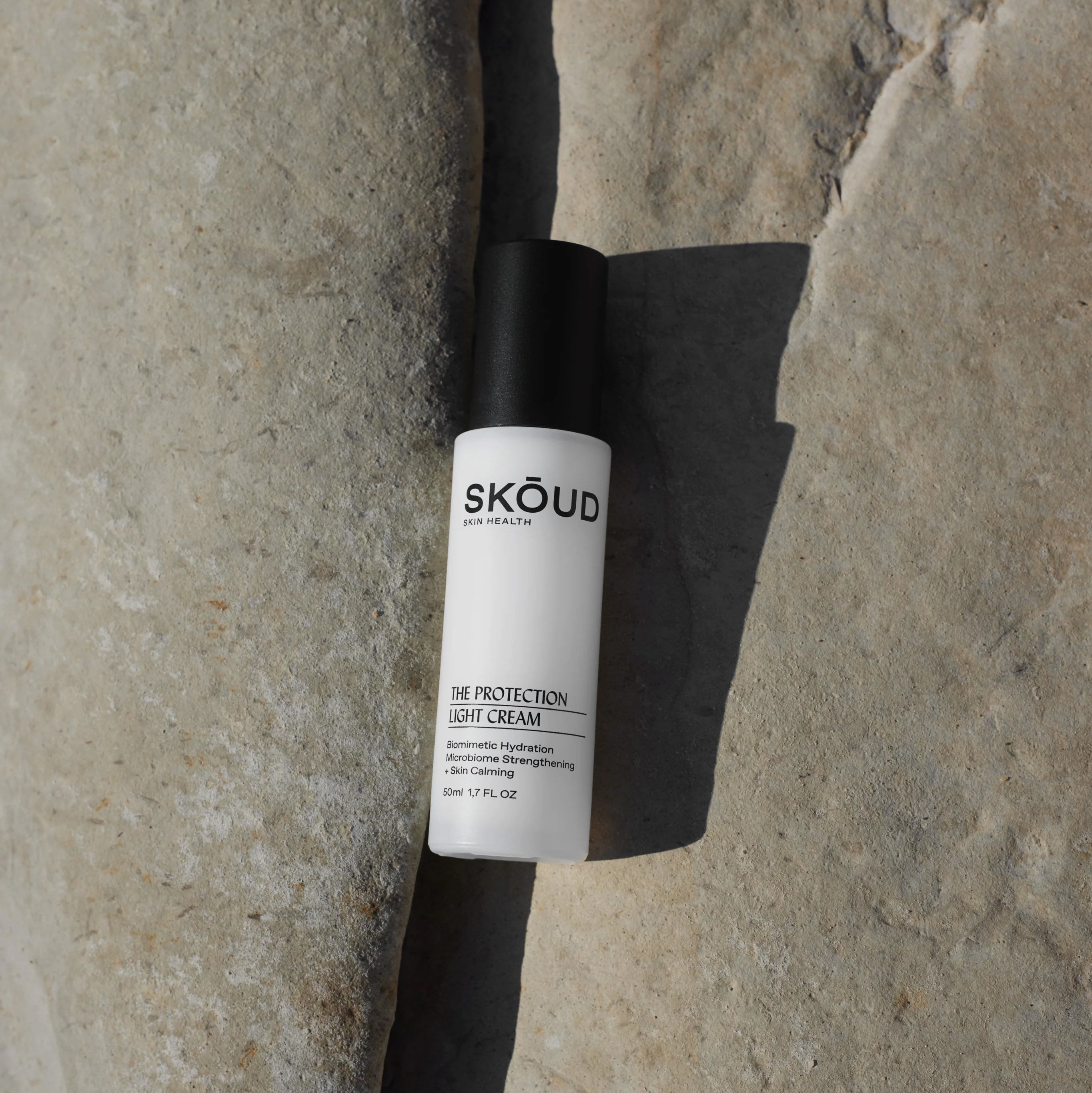 SKŌUD The Protection Light Cream Pumpflasche mit schwarzem Deckel liegt in einer Felsspalte.